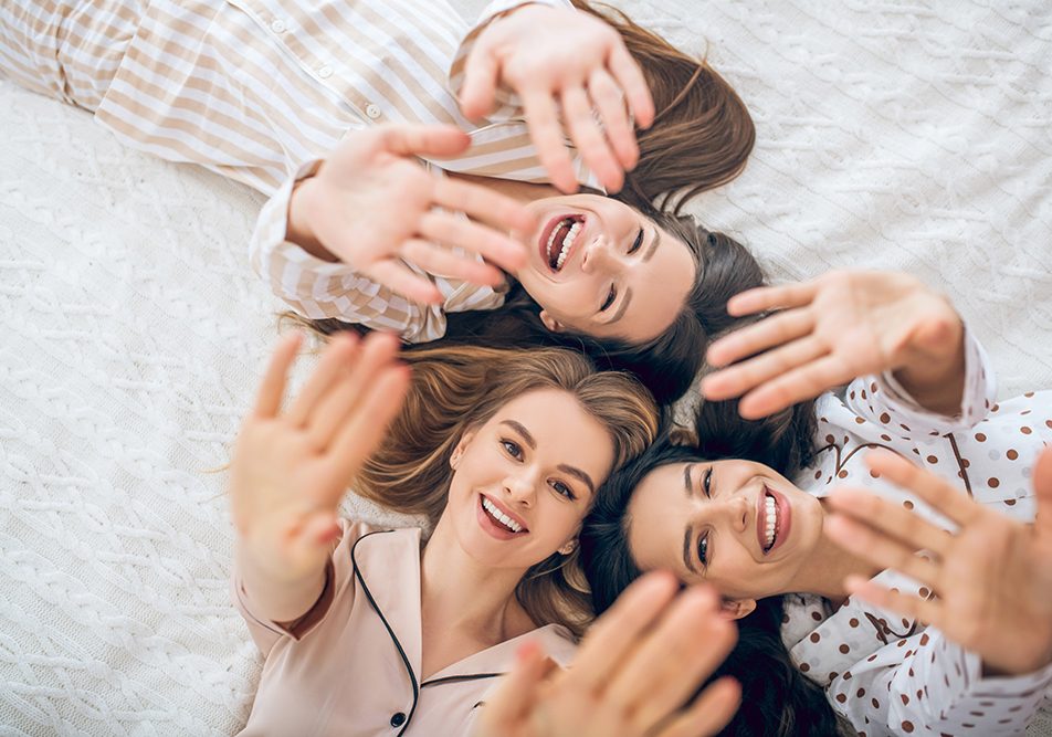 Un gruppo di amiche nel letto in pigiama che previene il rischio di infezioni intime adottando una corretta igiene intima e indossando biancheria di cotone