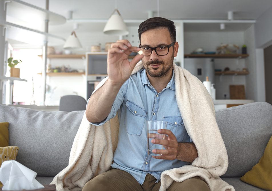 Uomo di età media indisposto che assume il farmaco Augumentin sul divano di casa