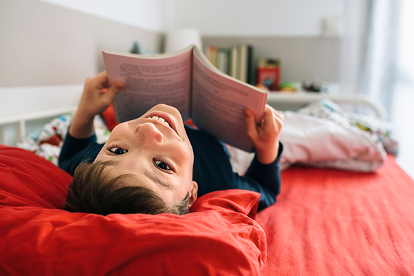 Bambino che legge un libro nel letto della sua cameretta durante il periodo di incubazione dello streptococco