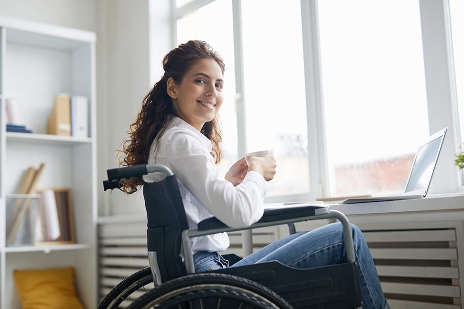 Donna sorridente affetta da sclerosi multipla che lavora al da remoto computer, mantenendo la sua autonomia