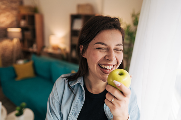 Giovane donna sorridente che mangia una mela per mantenere i suoi denti bianchi e in salute