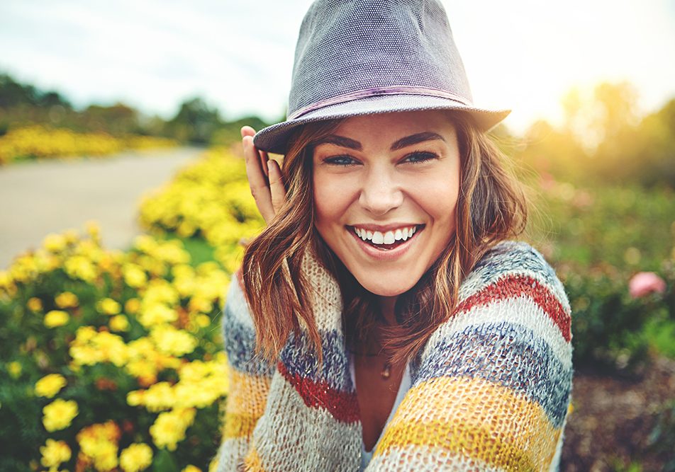 Giovane donna che sorride in un campo fiorito durante una giornata di primavera, che soffre di placche in gola senza febbre