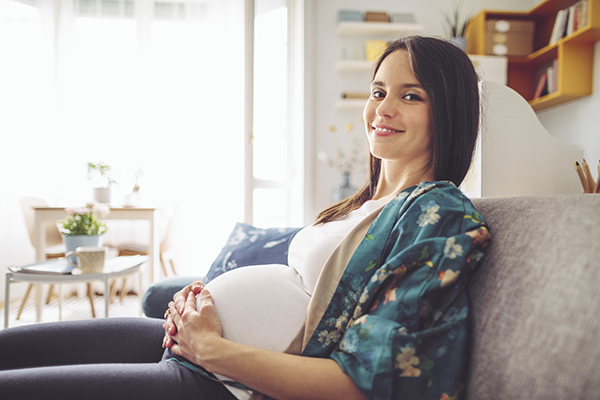 Donna sorridente in gravidanza, sul divano di casa, che accusa sintomi da streptococco