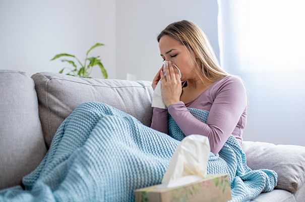 Donna sul divano di casa con tosse da infezione batterica in cura con amoxicillina