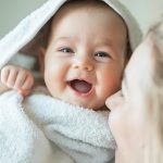 Madre che abbraccia la sua neonata sorridente, prevenendo la sesta malattia con l’adozione di buone pratiche di igiene