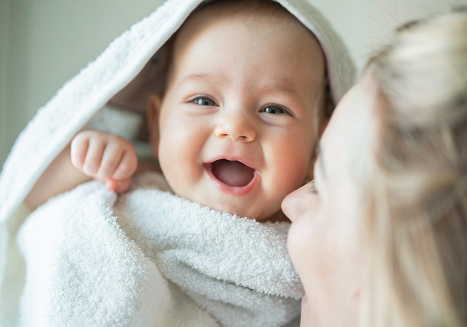Madre che abbraccia la sua neonata sorridente, prevenendo la sesta malattia con l’adozione di buone pratiche di igiene