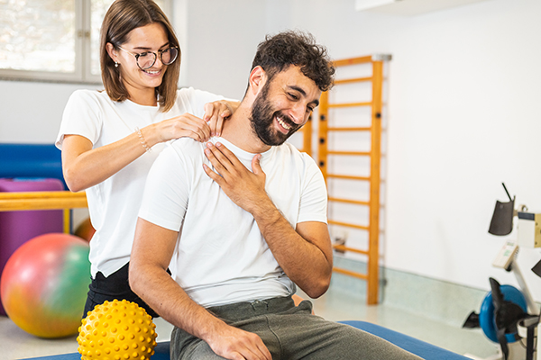 Paziente che pratica esercizi isometrici con il supporto della sua fisioterapista per il recupero da lussazione alla spalla