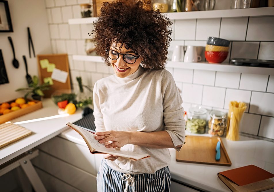 Giovane donna che consulta un ricettario per la preparazione di un pasto ricco di proteine vegetali