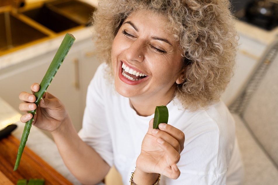 scabbia-rimedi-naturali-aloe-vera Donna sorridente dopo aver tagliato una foglia di aloe vera, rimedio naturale efficace contro la scabbia