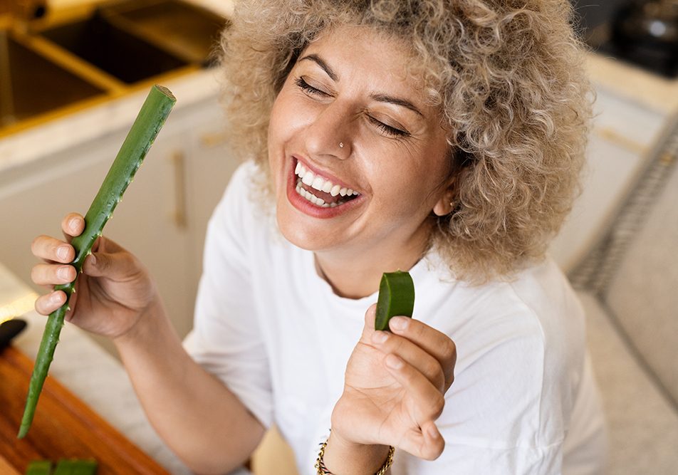 Donna sorridente dopo aver tagliato una foglia di aloe vera, rimedio naturale efficace contro la scabbia
