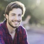 Giovane uomo sorridente seduto in un parco cittadino con placche in gola senza febbre