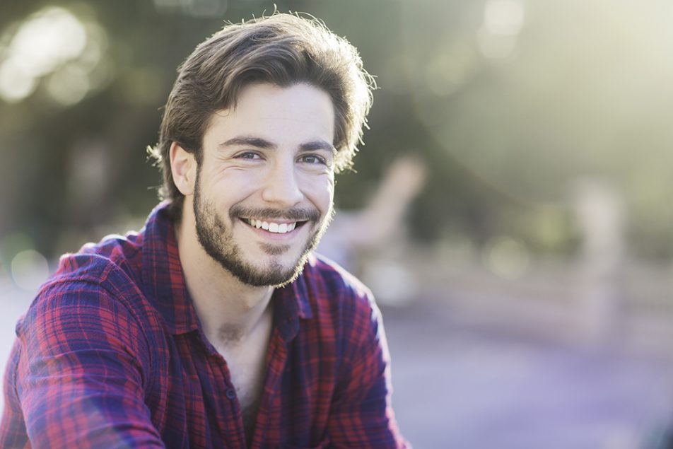 Giovane uomo sorridente seduto in un parco cittadino con placche in gola senza febbre