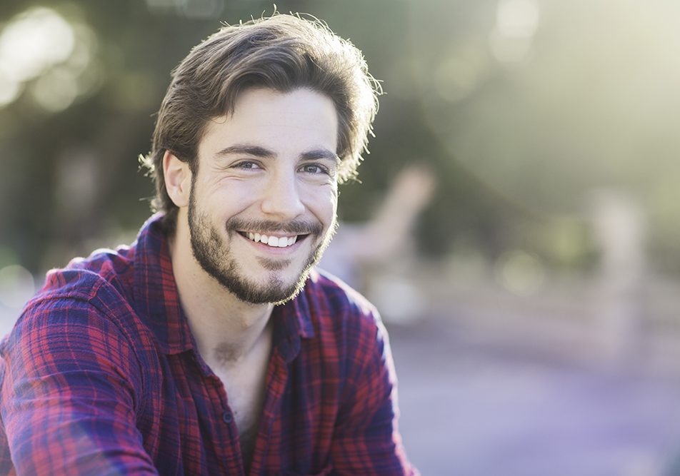 Giovane uomo sorridente seduto in un parco cittadino con placche in gola senza febbre