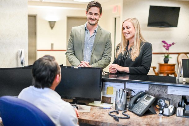 Coppia di mezza età che richiede informazioni sulle agevolazioni per disabili alla reception di un centro medico convenzionato