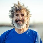 Uomo maturo sorridente dopo una camminata sulla spiaggia che previene lo streptococco grazie all’attività fisica all’aria aperta