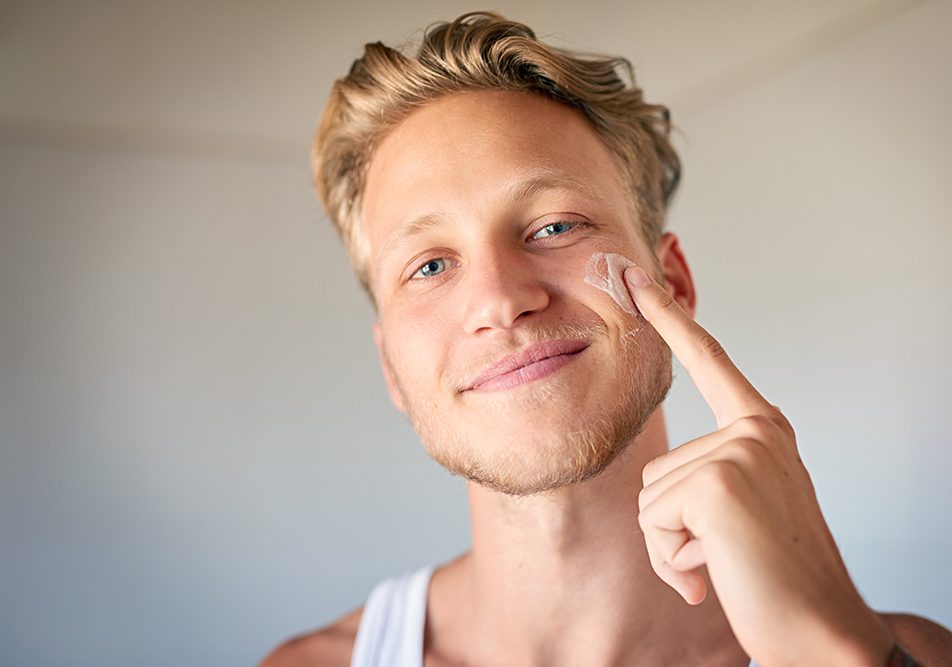 Giovane uomo che osserva davanti allo specchio l’infiammazione di un neo sul suo viso