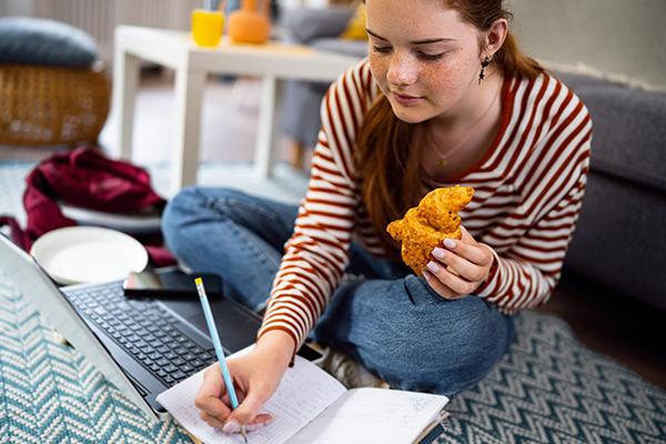 Adolescente che, mentre consuma un cornetto, tiene un diario alimentare e analizza davanti al computer come calcolare la massa grassa e i progressi della sua dieta