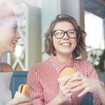 Giovani amiche che pranzano al fast food con un hamburger, a rischio di sviluppare una forma infantile e adolescenziale di obesità