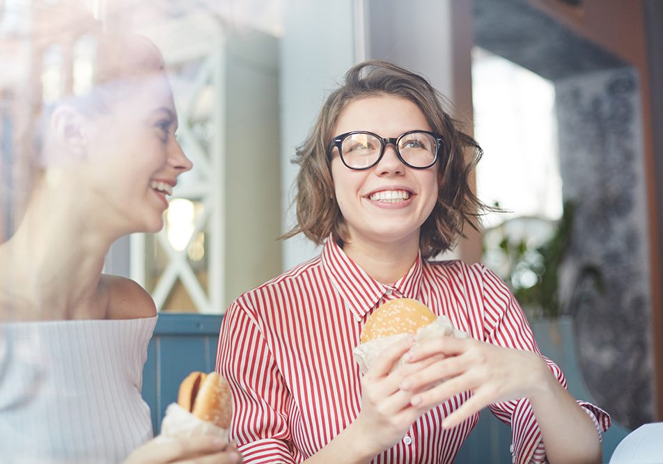 Giovani amiche che pranzano al fast food con un hamburger, a rischio di sviluppare una forma infantile e adolescenziale di obesità