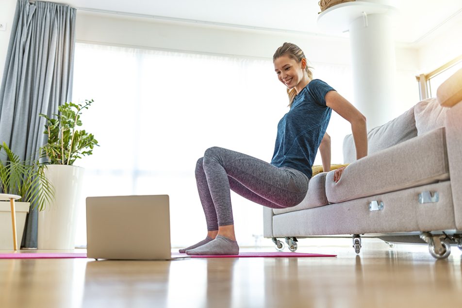 Donna che si allena a casa e osserva al computer un video tutorial sull’hip thrust