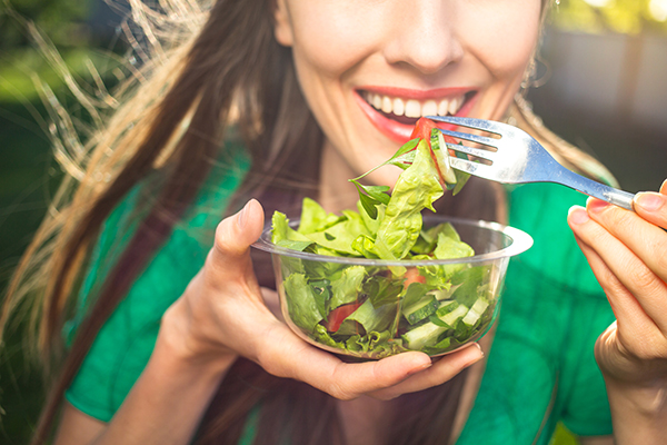 Donna che gusta un’insalata e affronta la sindrome premestruale primaverile seguendo una dieta equilibrata
