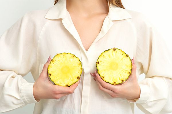 Donna che indossa una camicia e posiziona due fette di ananas a livello del suo seno e dei capezzoli