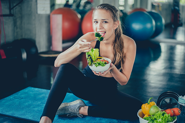 Donna sportiva che spezza la fame prima della palestra mangiando un’insalata con verdure di stagione