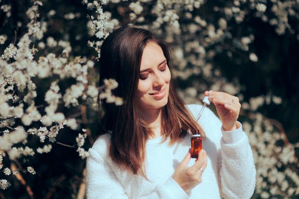 Donna in mezzo a fiori profumati che annusa una boccetta di oli essenziali