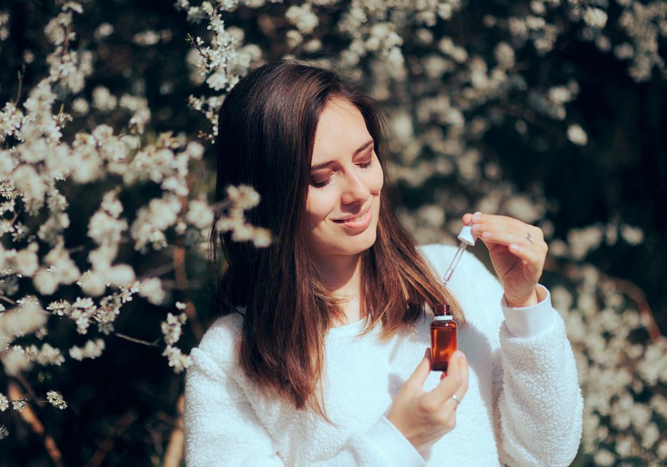 Donna in mezzo a fiori profumati che annusa una boccetta di oli essenziali