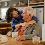 Figlia che abbraccia amorevolmente il padre nella cucina di casa, il quale ha patologie per cui beneficia dell’esenzione ticket