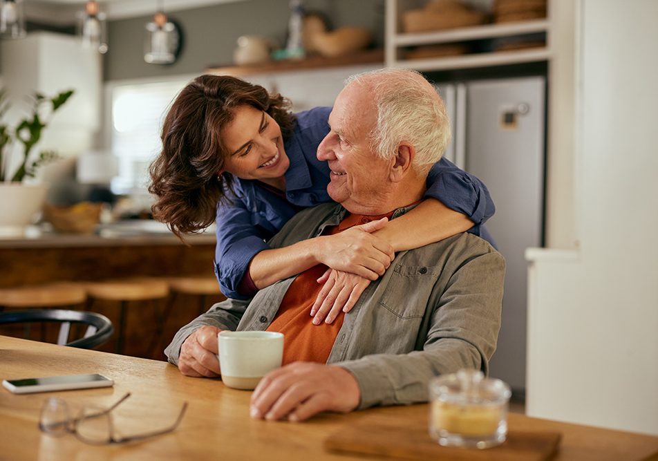 Figlia che abbraccia amorevolmente il padre nella cucina di casa, il quale ha patologie per cui beneficia dell’esenzione ticket