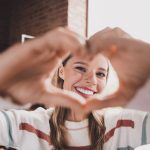 Giovane donna sorridente con sintomi delle coronarie ostruite che mostra alla camera il gesto del cuore