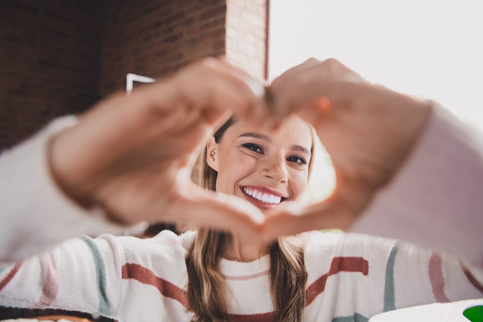 Giovane donna sorridente con sintomi delle coronarie ostruite che mostra alla camera il gesto del cuore