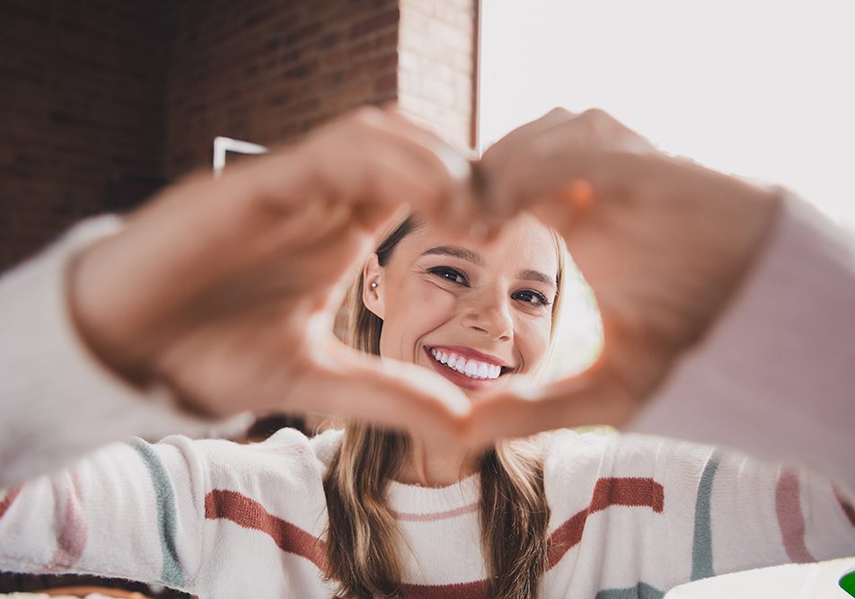 giovane-donna-con-coronarie-ostruite-sintomi-gesto-del-cuore Giovane donna sorridente con sintomi delle coronarie ostruite che mostra alla camera il gesto del cuore
