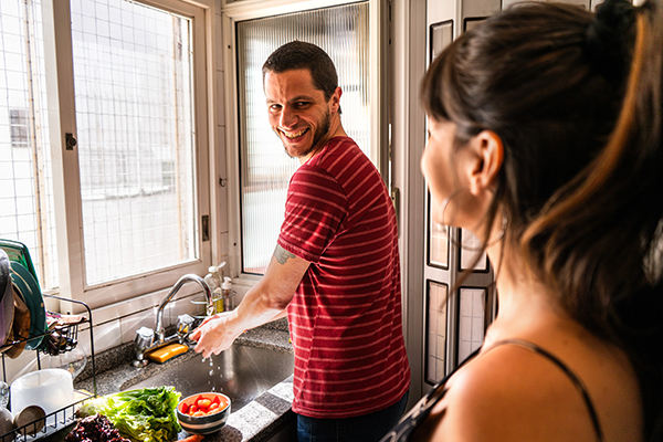 Giovane uomo che lava le verdure in cucina prevenendo l’ Helicobacter pylori e parlando alla sua compagna