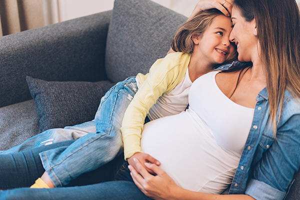 Madre in dolce attesa sul divano, che coccola la sua prima figlia già bambina, dopo il superamento dei primi sintomi della sua seconda gravidanza