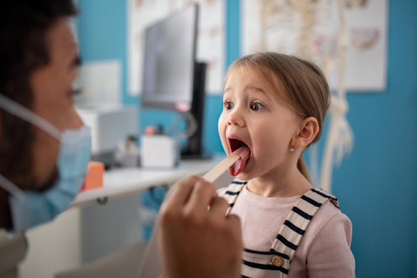 Giovane medico visita bambina con le placche in gola