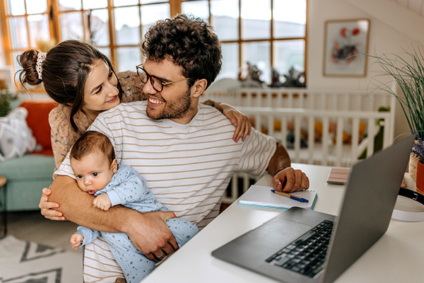Giovane padre al computer, insieme alla compagna e al bebè, che ricerca online informazioni sul rinnovo dell’esenzione ticket