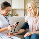 Paziente con sintomi di coronarie ostruite che misura la pressione nel salotto di casa con l’ausilio dell’infermiera