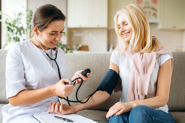 paziente-con-coronarie-ostruite-sintomi-misurando-pressione-con-infermiera Paziente con sintomi di coronarie ostruite che misura la pressione nel salotto di casa con l’ausilio dell’infermiera