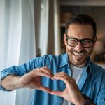 Uomo sorride facendo con le mani il segno del cuore dopo intervento coronarografia