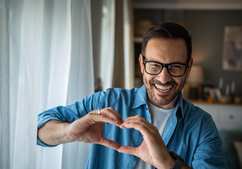 Uomo sorride facendo con le mani il segno del cuore dopo intervento coronarografia