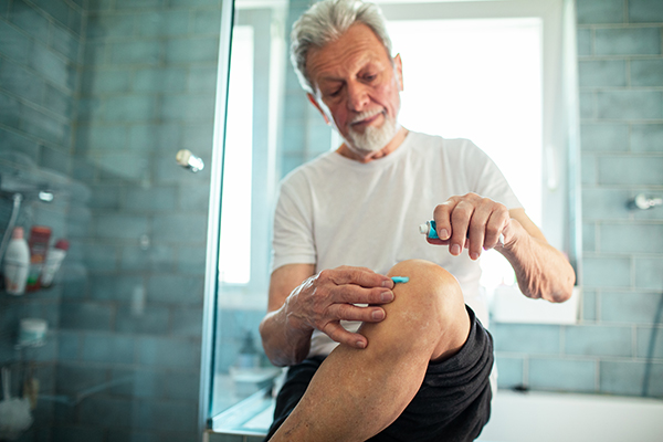 Uomo che segue la terapia per la cura dell’erisipela applicando una pomata analgesica sulla gamba
