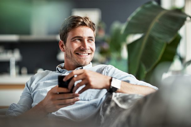 uomo-sul-divano-di-casa-prenotando-check-up-medico-dallo-smartphone Uomo seduto rilassato sul divano di casa che prenota un check-up medico direttamente dal suo smartphone