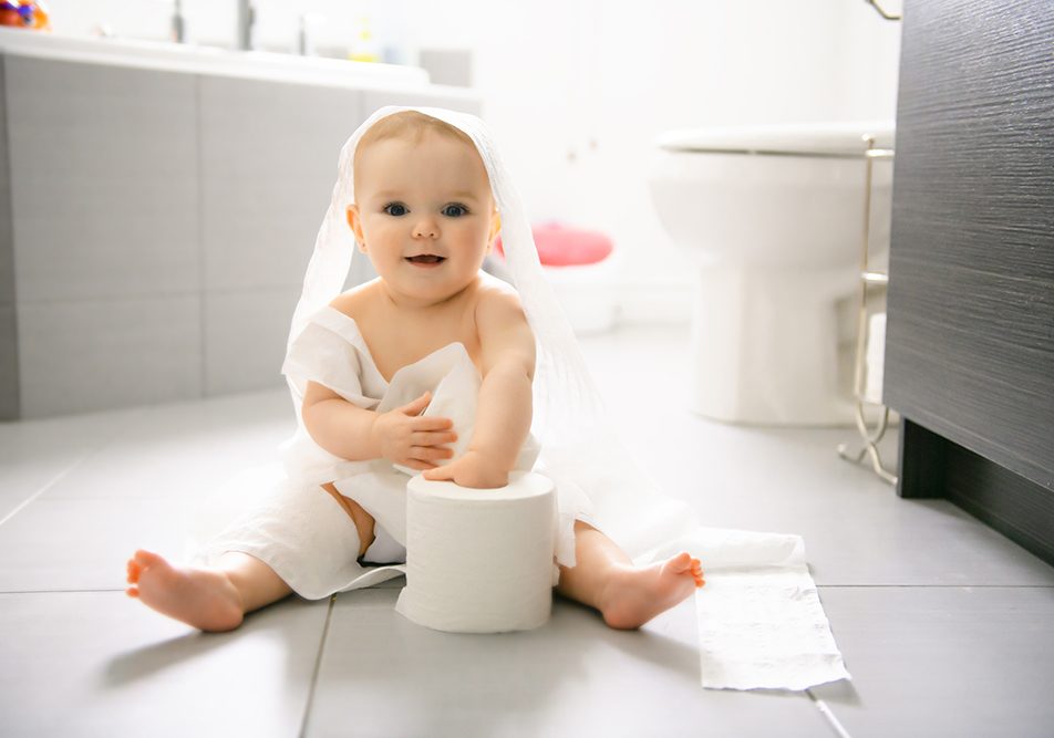 diarrea-neonato-in-bagno-strappando-carta-igienica Neonato con diarrea seduto sul pavimento di un bagno moderno, mentre gioca con i rotoli di carta igienica e ne strappa alcuni fogli