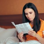 Donna influenzata seduta a letto che legge il foglietto illustrativo dell’Oki prima di assumerlo