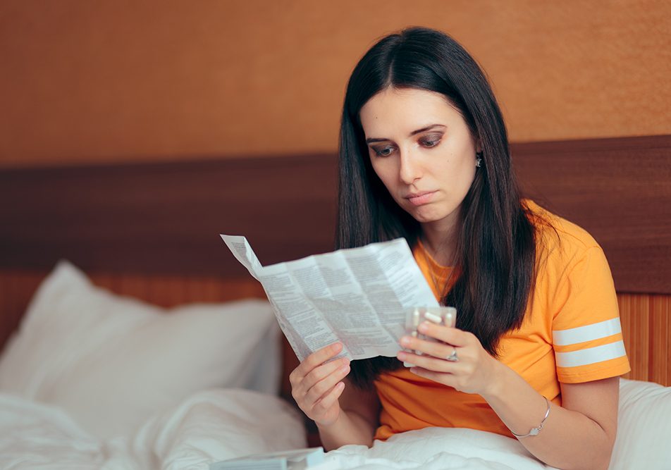 Donna influenzata seduta a letto che legge il foglietto illustrativo dell’Oki prima di assumerlo