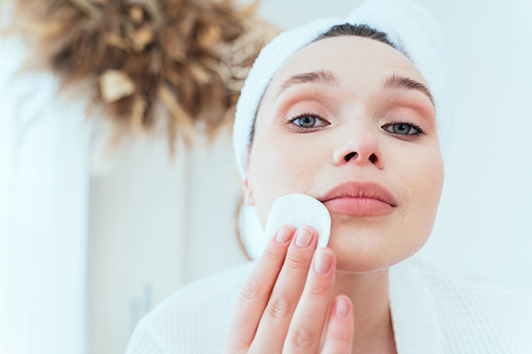 Donna che indossa accappatoio e asciugamano turbante per capelli che applica un dischetto di cotone per esfoliare le sue labbra carnose