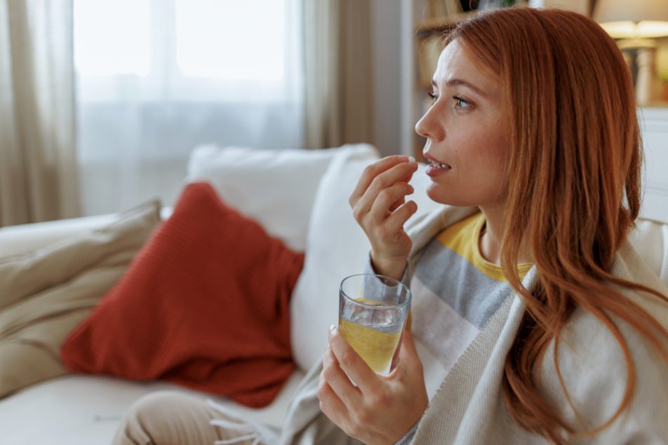 Giovane donna, seduta sul suo divano, che prende Oki a stomaco vuoto
