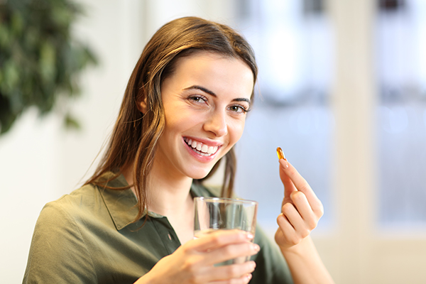 Donna con bicchiere d’acqua in mano che mostra una capsula di integratore Omega 3 suggeritole dal medico